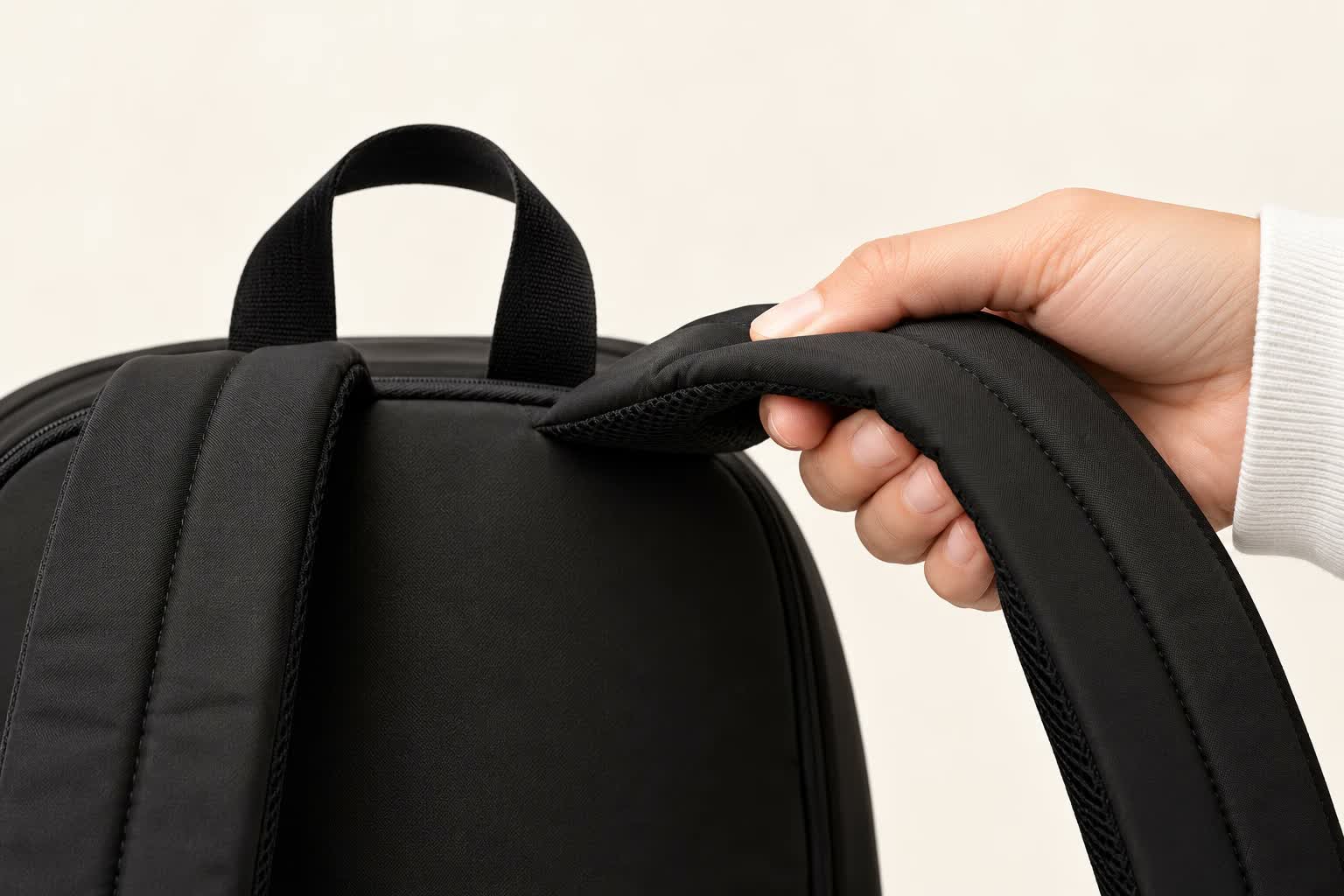 A hand pressing on the backpack's padded, contoured shoulder strap.